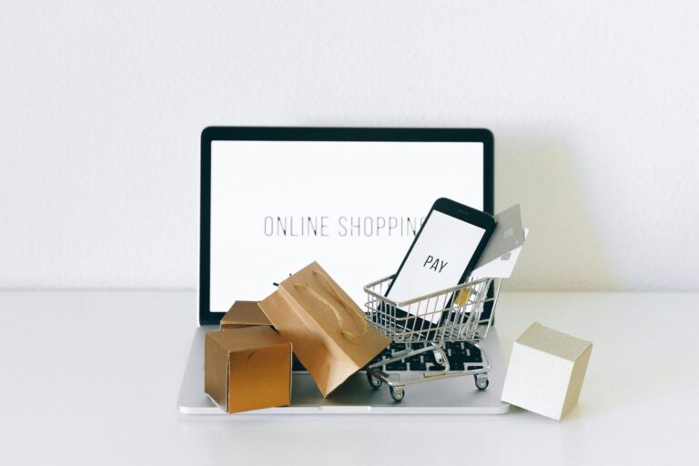 Notebook com a tela de uma loja virtual, carrinho de compras em miniatura com caixas e celular na tela de pagamento