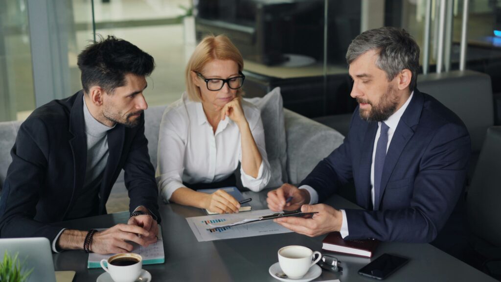 Dois empresários em mesa de reunião formal assinam documentos jurídicos corporativos enquanto analisam riscos contratuais quando o sócio quer vender quotas para terceiros.