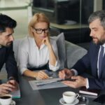 Dois empresários em mesa de reunião formal assinam documentos jurídicos corporativos enquanto analisam riscos contratuais quando o sócio quer vender quotas para terceiros.